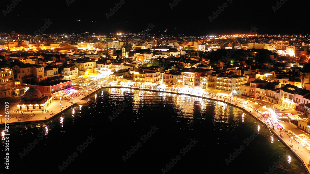 Aerial drone night shot of iconic and picturesque illuminated Venetian old port of Chania with famous landmark lighthouse and shops - restaurants serving Cretan traditional food, Crete island, Greece
