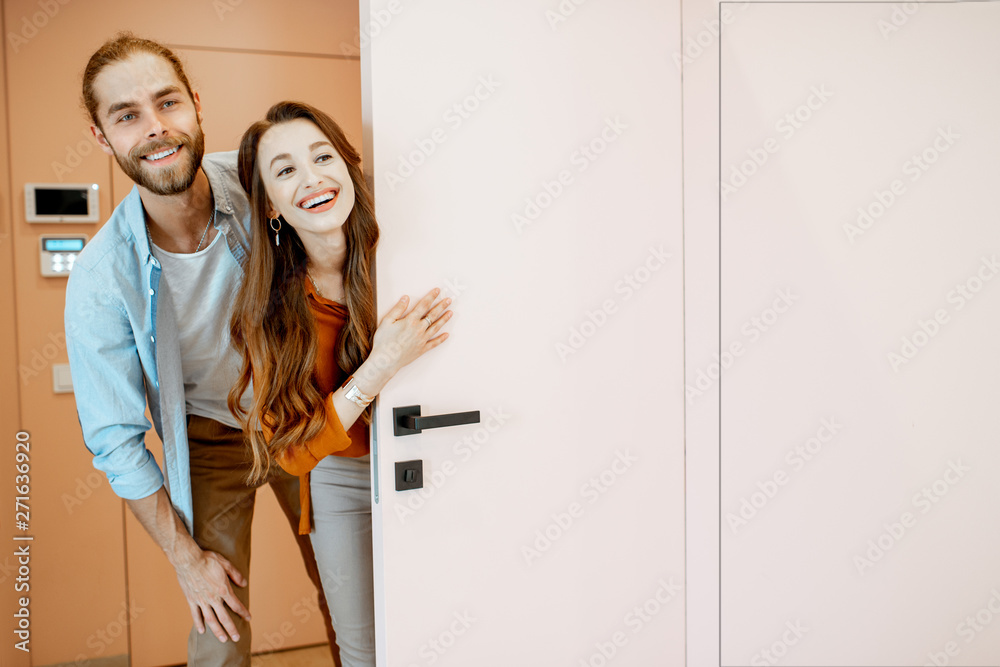 Portrait of a young couple looking out the door at the corridor of the new modern apartment. Concept of happy real estate owners Portrait of a young couple looking out the door at the corridor of the new modern apartment. Concept of happy real estate owners