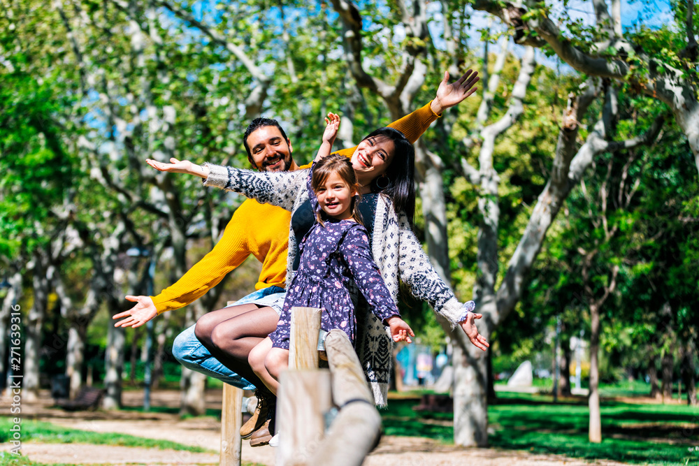 Front view of a happy arms raised family enjoying at park while looking camera and smiling in a sunny day