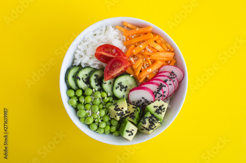 Vegan poke bowl with white rice and vegetables in the white bowl in the center of the yellow background.Top view.Closeup.