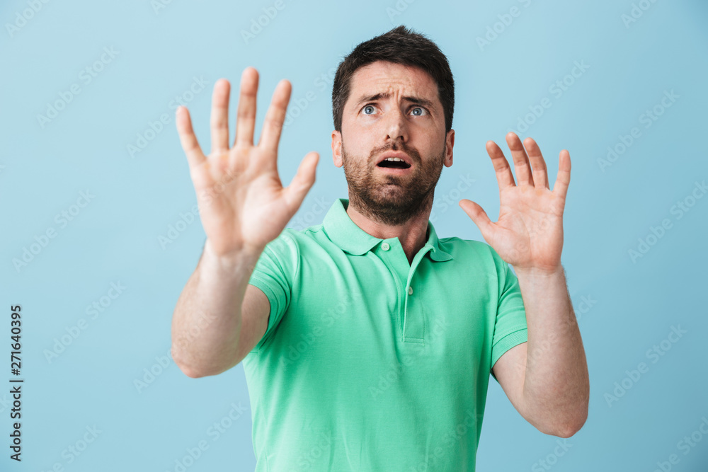 Scared confused young handsome bearded man posing isolated over blue wall background covering mouth. Scared confused young handsome bearded man posing isolated over blue wall background covering mouth.