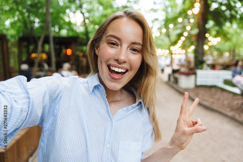 Amazing excited happy young woman posing outdoors in park take a selfie by camera.