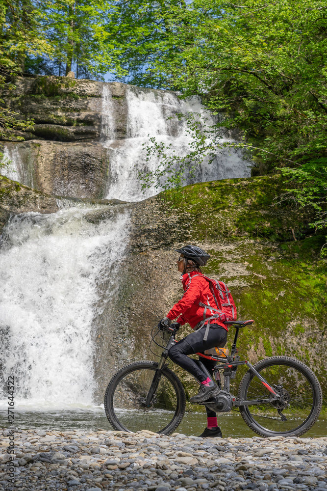 senior woman, underway with her e mountain bike, looking at a waterfall in the Allgaeu Alps, Bavaria,Germany