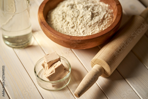 Top view of bowl of flour with yeast and rolling pin on  white  kitchen table