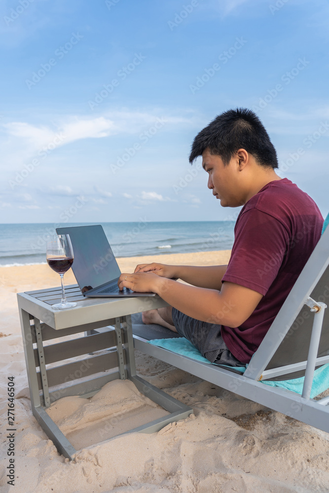 Asian man typing laptop with glass of wine on beach