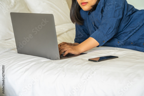 Woman laying on bed and using laptop next to cellphone