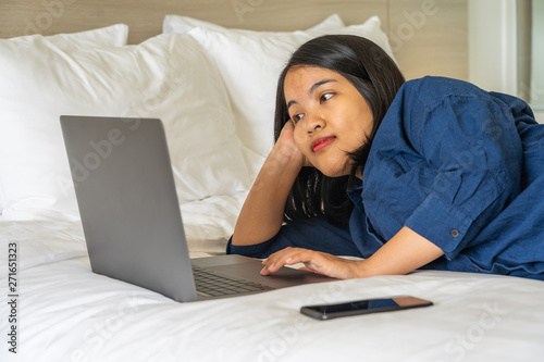 Young woman laying on bed and using laptop