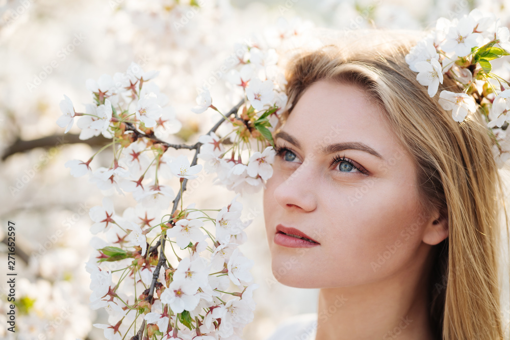 Attractive lady smiling and looking at camera while standing near tree branches blooming with white flowers Attractive lady smiling and looking at camera while standing near tree branches blooming with white flowers
