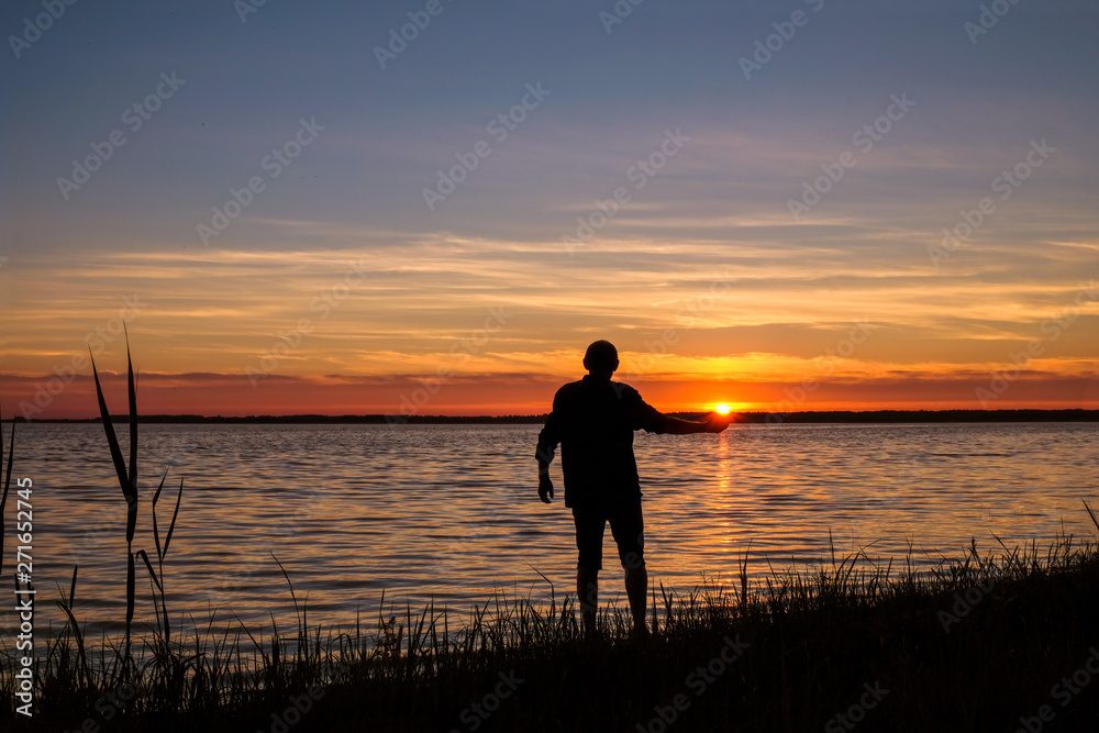 The man 58 years old on the shore of Svityas Like admires the sunset in the summer in Ukraine. The sun is on the man's palm. Self-isolation concept.