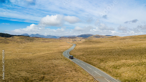 Back view of automobile riding on lonely asphalt road in mountain terrain in sunny day in Wales photo