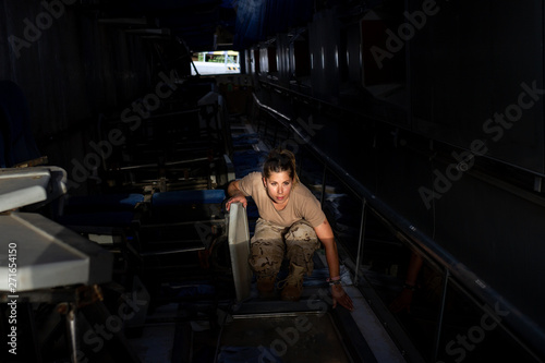 Side view of strong female soldier pointing up while looking at sky through ceiling window of military base photo