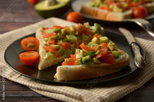 Healthy toast with avocado, cherry tomatoes and cheese on a plate. Wooden table.