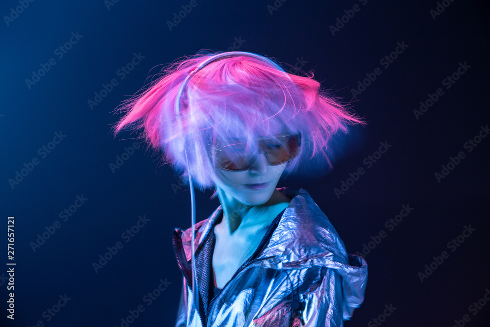 Young subcultural Asian woman with pink scattered hair and silver jacket dancing while listening to music in headphones Young subcultural Asian woman with pink scattered hair and silver jacket dancing while listening to music in headphones