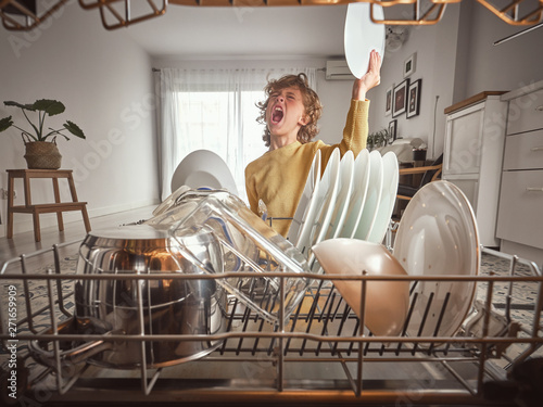 Little boy with wavy hair yawning while standing near open dishwasher in early morning in kitchen photo