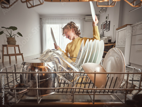 Little boy with wavy hair yawning while standing near open dishwasher in early morning in kitchen photo