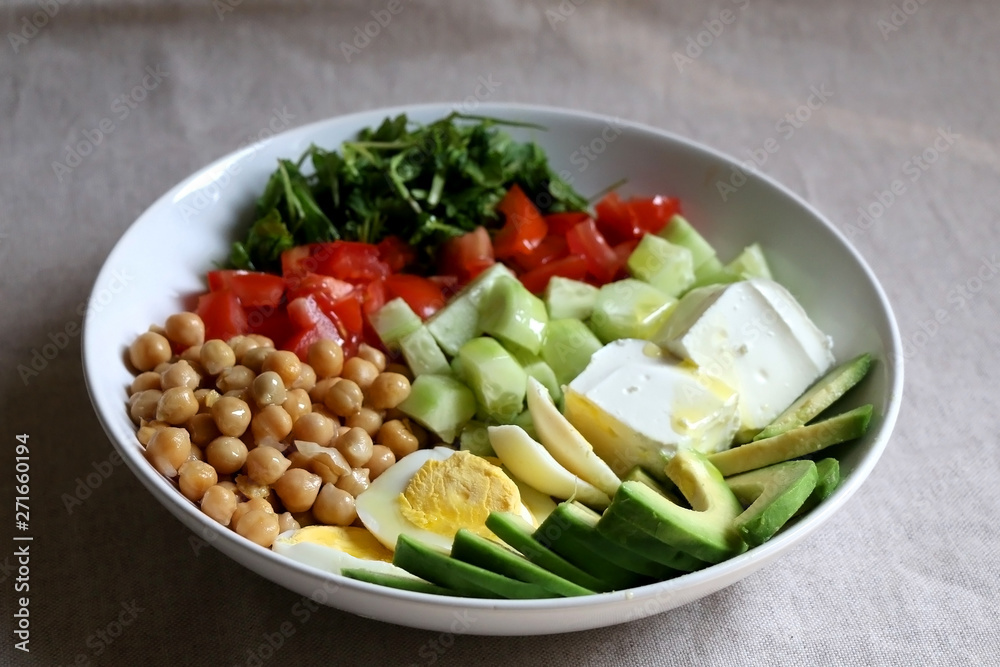 Lunch bowl with avocado, hard boiled egg, chickpea, feta cheese, cucumber, tomato and arugula. Selective focus.