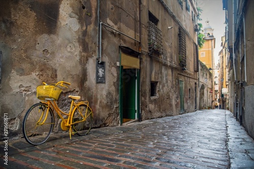 Street view of an ancient narrow alley   caruggio  in Genoese  in the historic centre of Genoa with a yellow bicycle parked against a scraped wall and the pavement of stones and bricks  Liguria  Italy