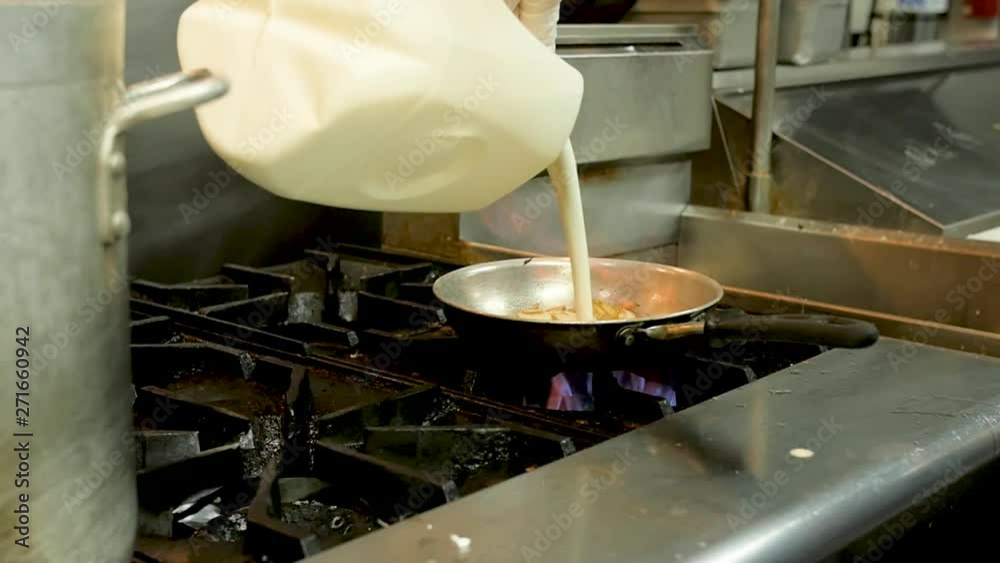chef pours cream into pan on professional stove slow motion. A chef pours cream into a sauce pan as it cooks on a gas stove in a professional kitchen. chef pours cream into pan on professional stove slow motion. A chef pours cream into a sauce pan as it cooks on a gas stove in a professional kitchen.