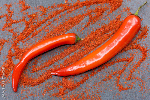 Raw red chili peppers and ground paprika on dark slate plate as background. Natural stone textured background. Flat lay