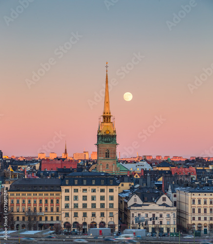Full moon in rising behind the Old German Church tower (Tyska Kyrkan) on Gamla Stan island in orange and pink sky at sunset in Stockholm, Sweden.