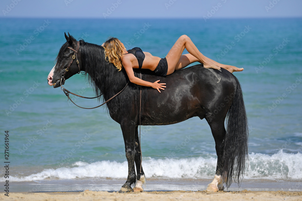 Portrait of a beautiful blond girl lies on the back of her black horse on the Rishpon beach, Israel Portrait of a beautiful blond girl lies on the back of her black horse on the Rishpon beach, Israel