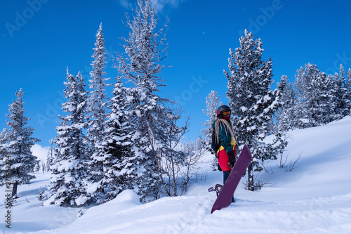 Woman freerider with snowboard on a snowy slope among the Alpine Christmas trees.