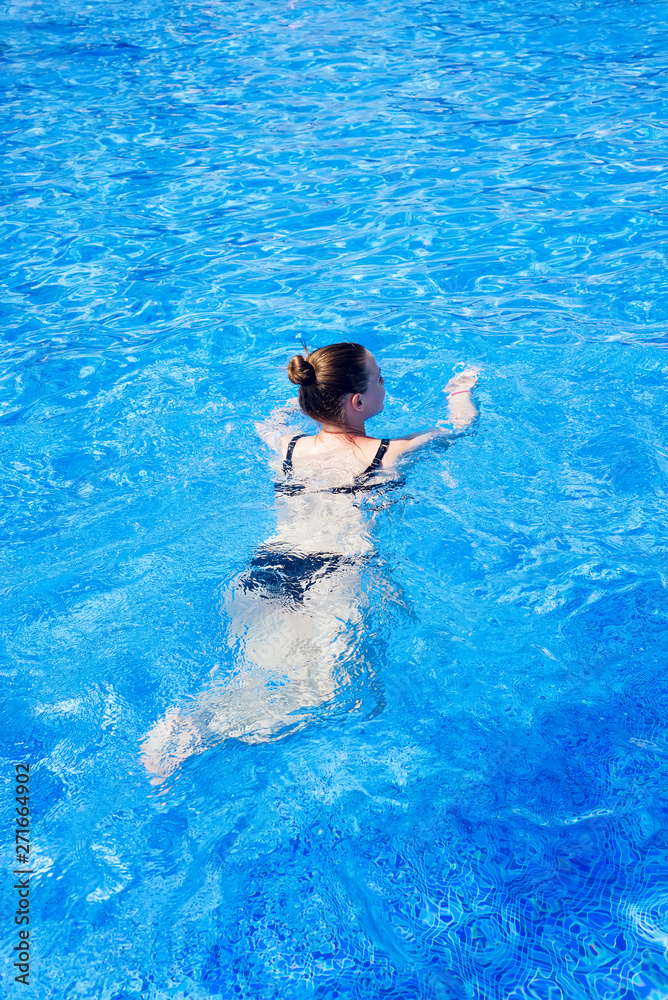 woman with swimsuit swimming on a blue water pool, tropical vacation holiday concept