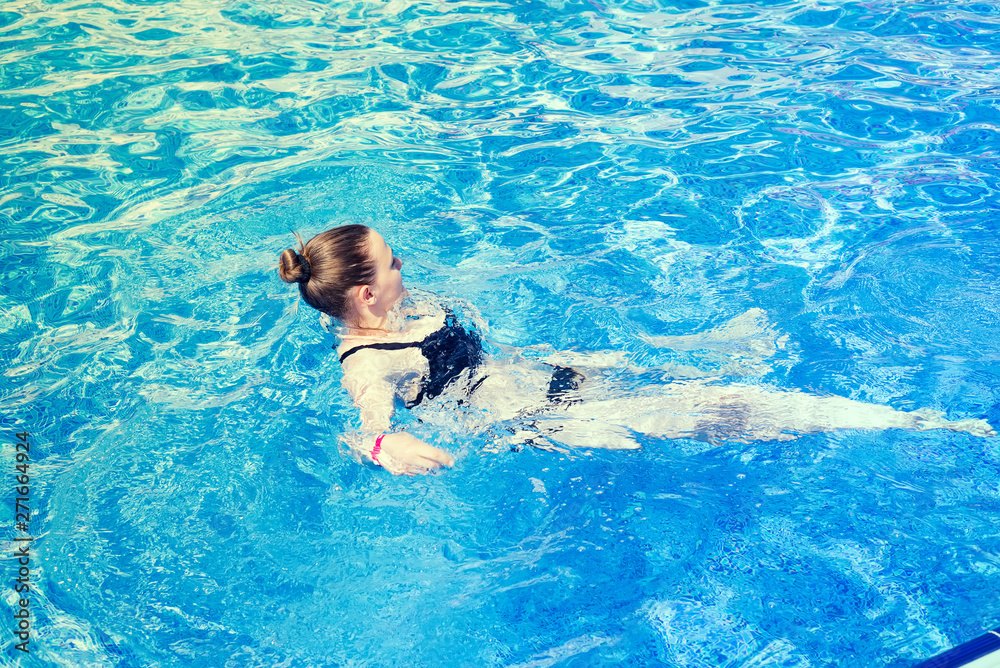 woman with swimsuit swimming on a blue water pool, tropical vacation holiday concept