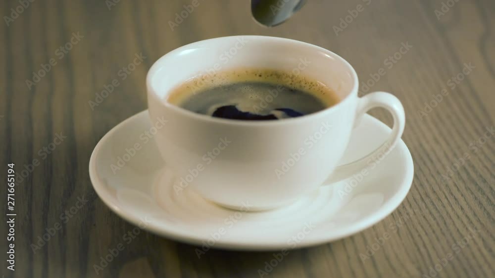 In a cup of coffee, a spoon of sugar is added and it is stirred.