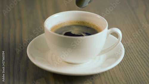 In a cup of coffee, a spoon of sugar is added and it is stirred.