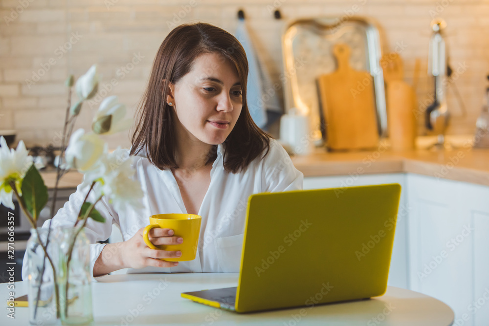 young pretty caucasian woman talking on the phone sitting in front of laptop in the kitchen young pretty caucasian woman talking on the phone sitting in front of laptop in the kitchen
