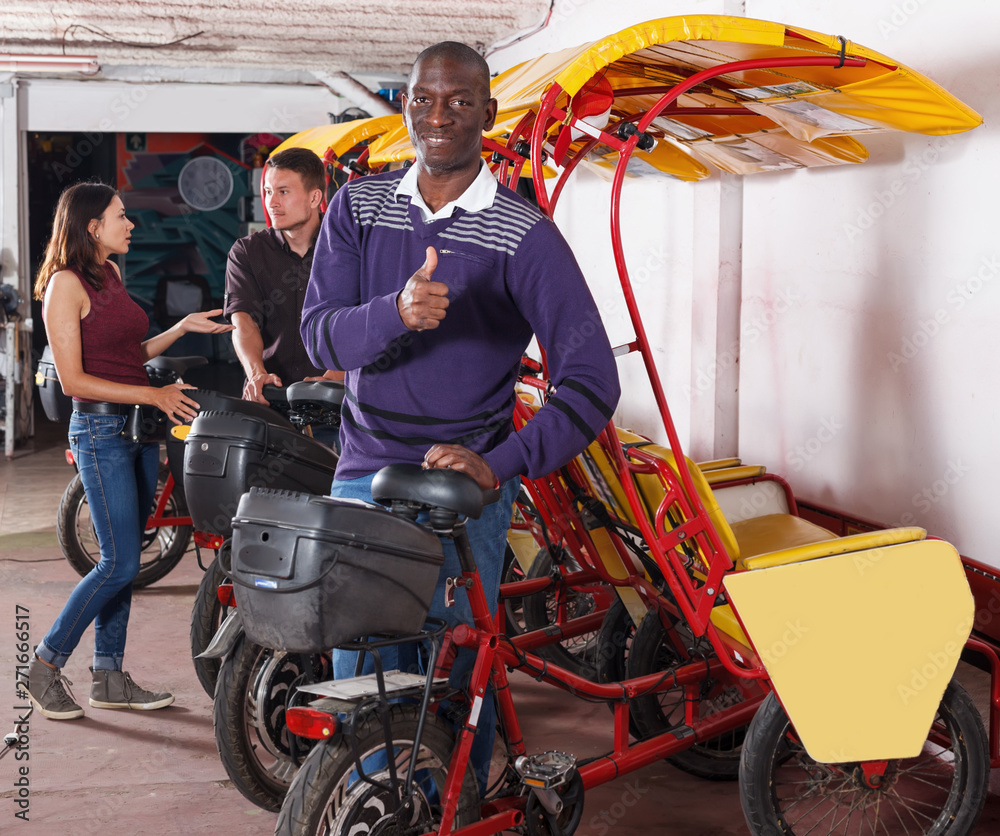 African-American man pedicab driver standing near rickshaw cycle