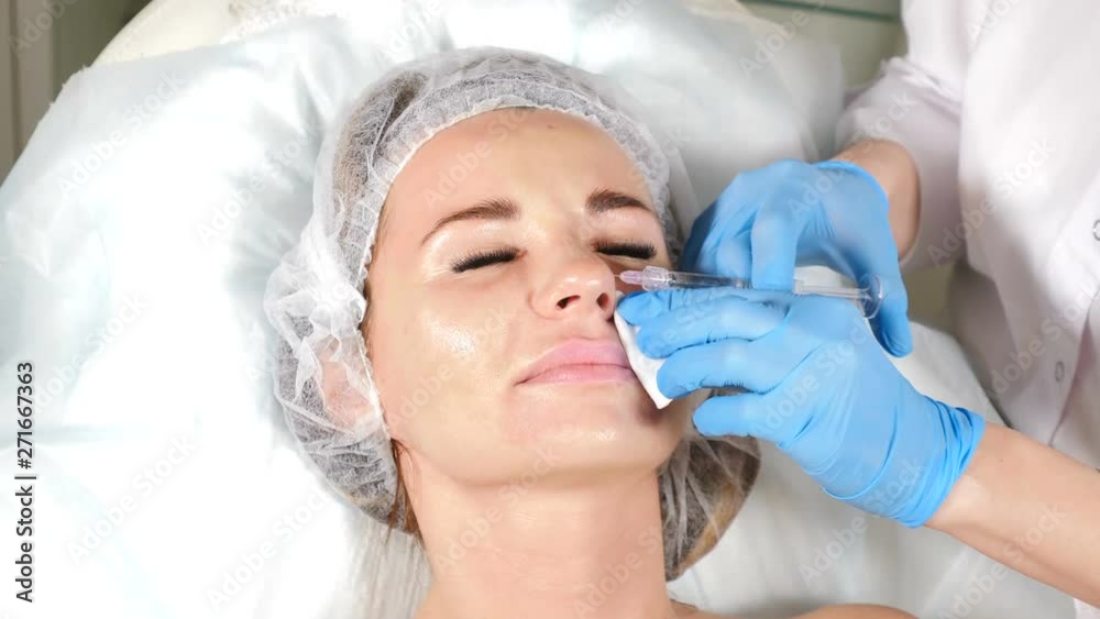 Non-surgical correction of shape of nose. A young girl during beauty procedure. Close up of beautician hands in blue gloves making injections to nose. 4k Non-surgical correction of shape of nose. A young girl during beauty procedure. Close up of beautician hands in blue gloves making injections to nose. 4k