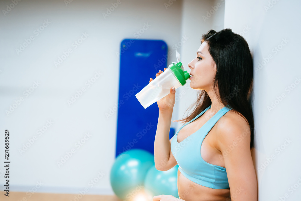 Sportswoman resting and drinking water on stairs in gym Sportswoman resting and drinking water on stairs in gym