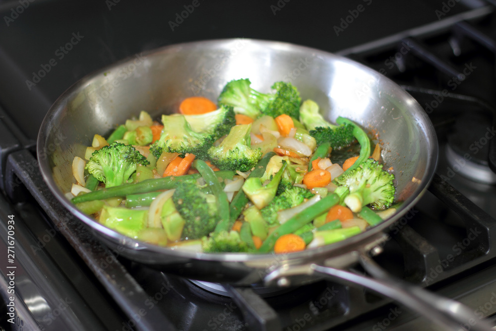 Stir fry vegetables cooking in a stainless steel pan on a natural gas stove. Stir fry vegetables cooking in a stainless steel pan on a natural gas stove.