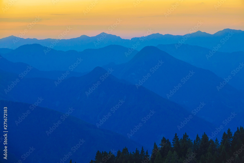 AERIAL: Vibrant yellow and blue evening sky spans above the mountain range.