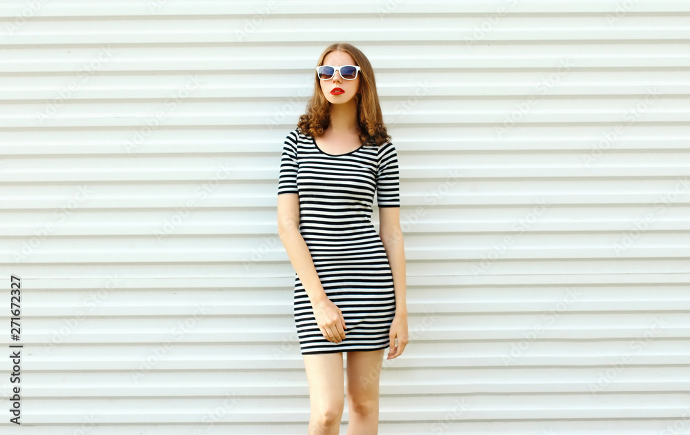 Stylish young woman in striped dress posing on white wall background Stylish young woman in striped dress posing on white wall background