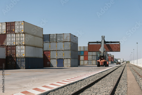 Crane lifting cargo container near railway tracks on industrial site photo