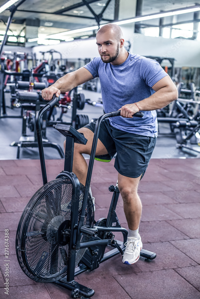 young man using exercise bike at the gym. Fitness male using air bike for cardio workout at crossfit gym. young man using exercise bike at the gym. Fitness male using air bike for cardio workout at crossfit gym.