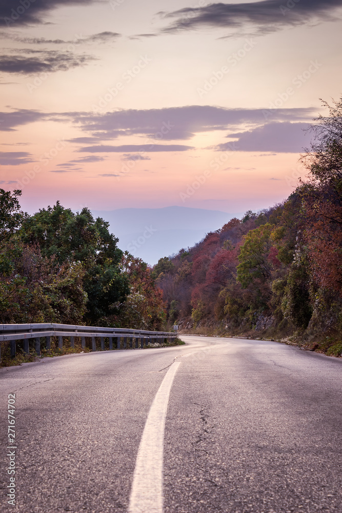 Curvy mountain road with white line, autumn colors and beautiful sunset sky and sunlit rocks