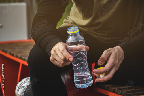 young man in sportsweaat gym holding bottle of water on the sports field