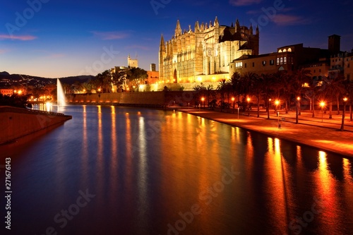 Palma cathedral illuminated at dusk with lake, fountain and reflections on water, mallorca, spain.