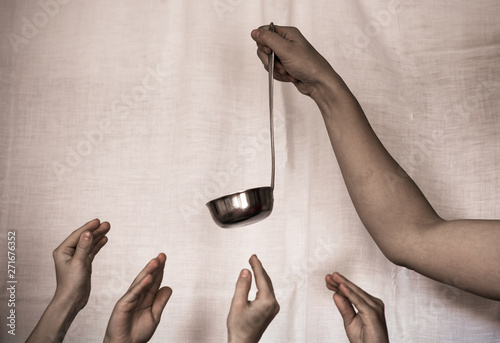 The hand of an adult holding a ladle, children's hands reach for it