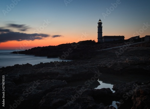 Lighthouse Far del cap ses salines at sunset, rocks, building, setting sun, beautiful golden sky, Mallorca, Spain.