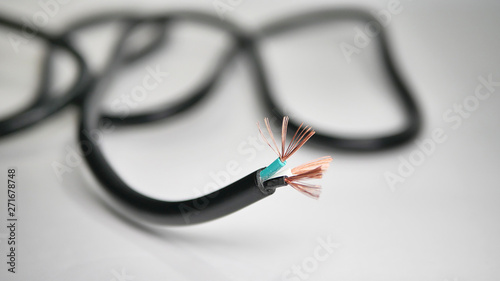 A close-up shot of a black power cord with stripped end showing green, black, and white wires with copper strands spread out.