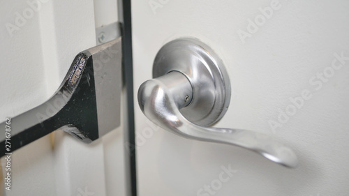 A white door ajar with brushed nickel lever handle.  A black pry bar is being used to force open the door for a home invasion, robbery or crime.