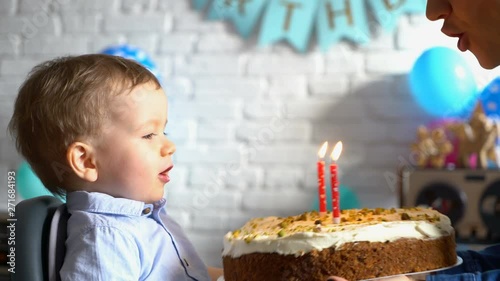 Mother helping her little son blowing out candle on a birthday cake