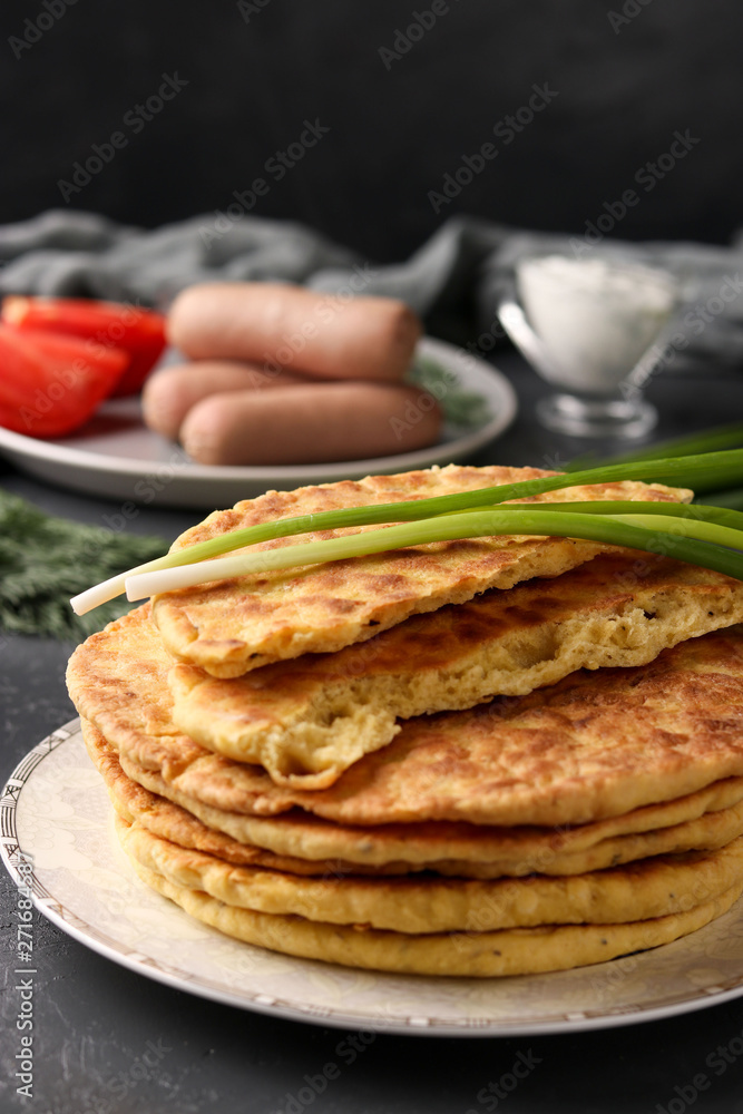 Homemade tortillas, located on a plate on a dark background, in the background sour cream, sausages and tomatoes Homemade tortillas, located on a plate on a dark background, in the background sour cream, sausages and tomatoes
