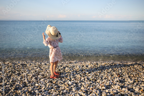 Funny girl in tunic and a big hat on pebble beach