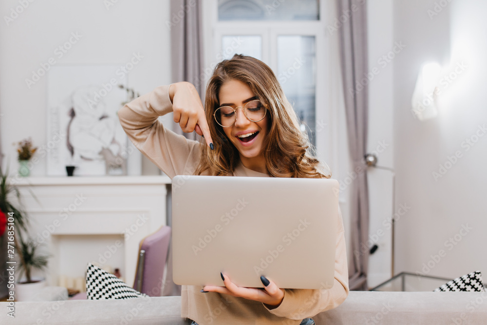Interested girl with trendy manicure fooling around at home during photoshoot with laptop. Indoor photo of graceful smart woman in glasses holding computer with smile. Interested girl with trendy manicure fooling around at home during photoshoot with laptop. Indoor photo of graceful smart woman in glasses holding computer with smile.